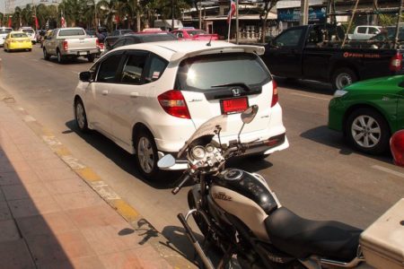 タイの道路で赤プレートのホンダJAZZと警察バイクが並ぶ停車シーン
