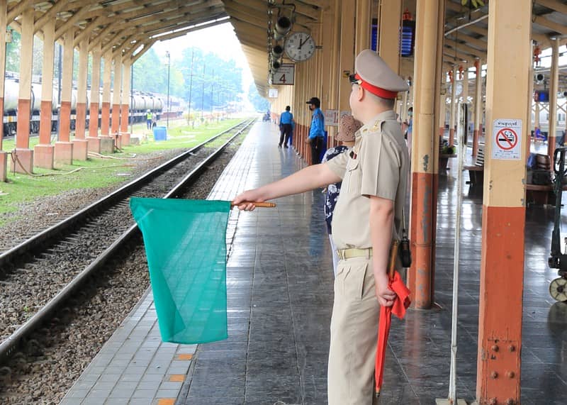 チェンマイ駅で緑と赤の旗を使い列車誘導を行う駅員の姿